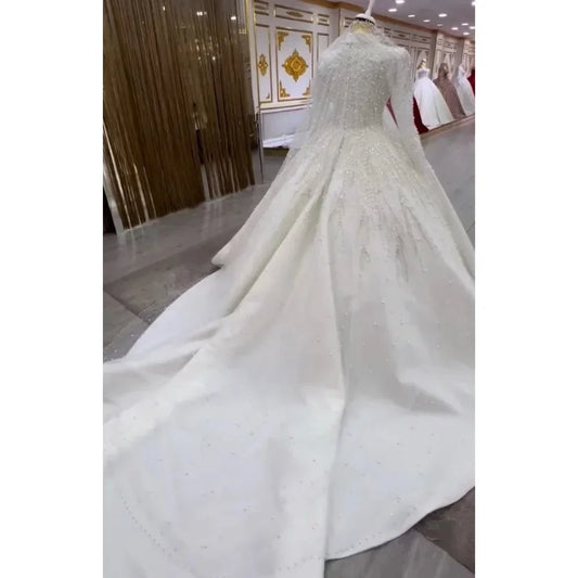 Elegant white wedding gown with long sleeves, beaded details, and a flowing train displayed in a boutique.