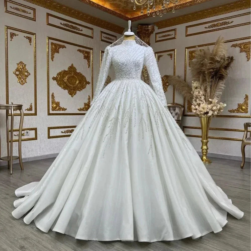 Elegant white wedding gown with long sleeves, beaded bodice, and full ball gown skirt displayed in luxury setting